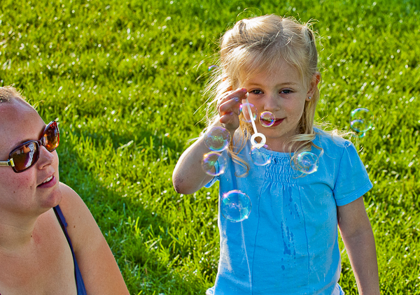 Mother watches daughter blow soap bubbles during concert at Leather Commons