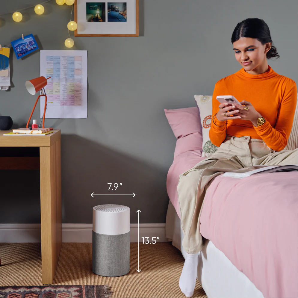 girl sits on bed reading with small air purifier on floor